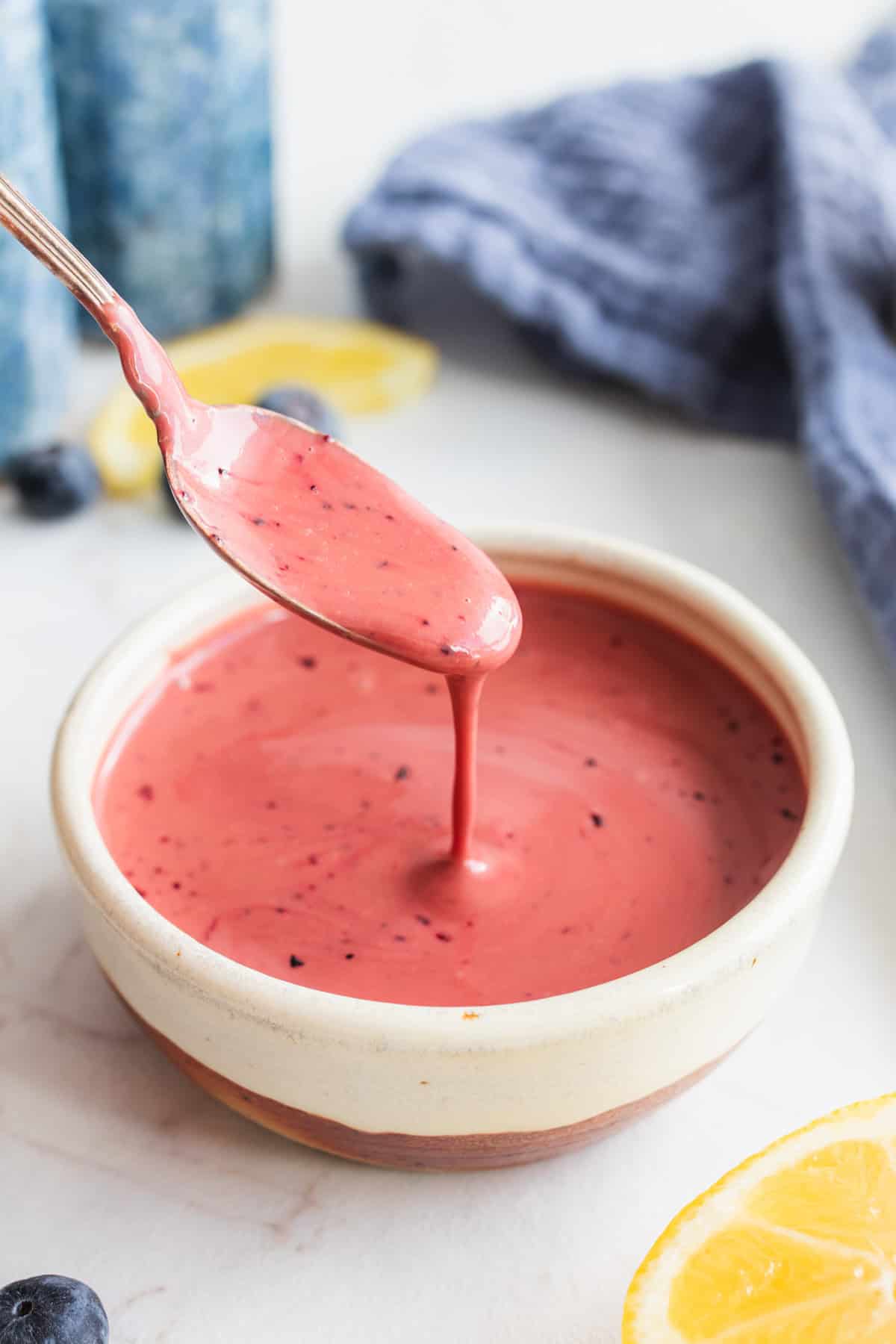 Blueberry vinaigrette in a small bowl drizzling off a spoon.