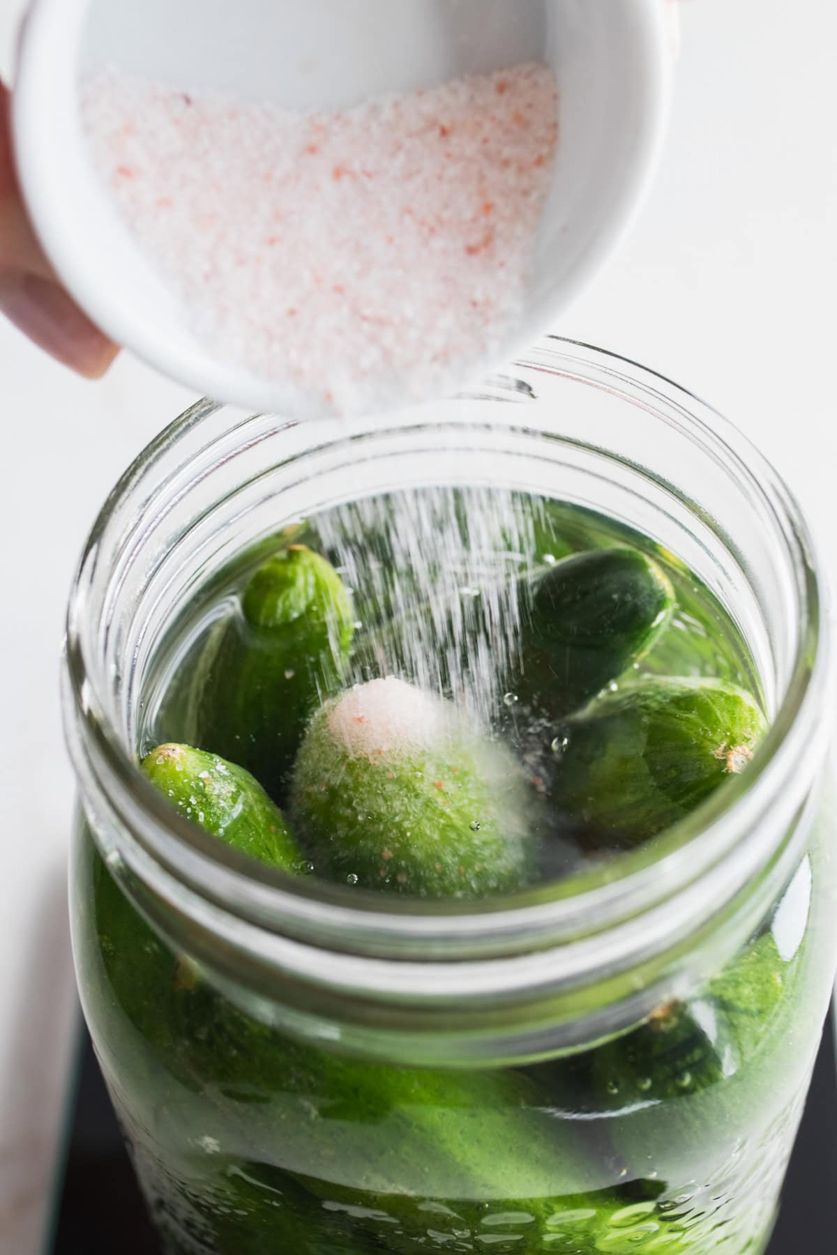 Salt added to a jar of cucumbers and water.