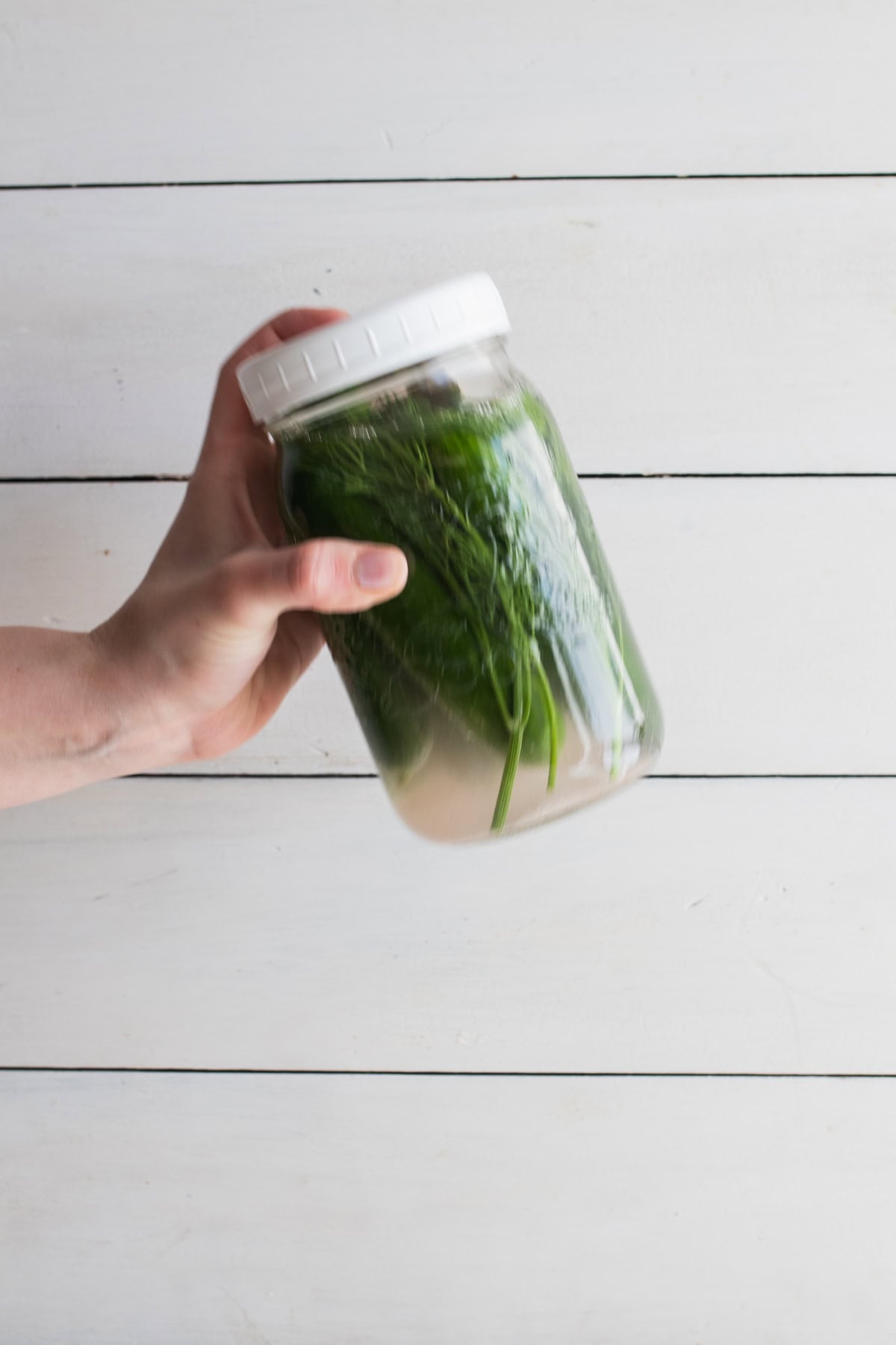 A hand shaking a jar of cucumbers and water.