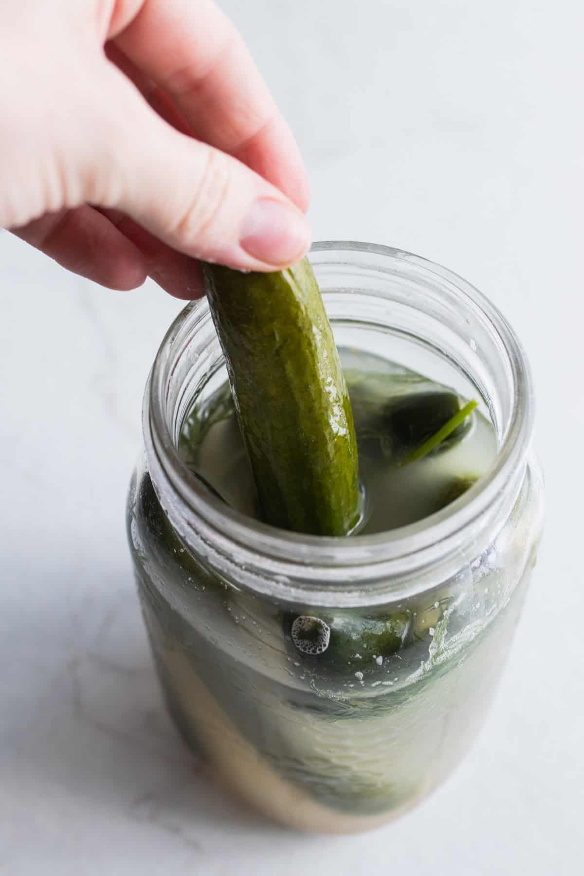 A hand taking a pickle out of a jar.