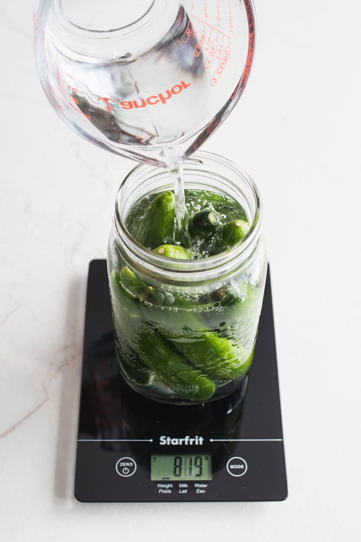 Water added to a jar of cucumbers.