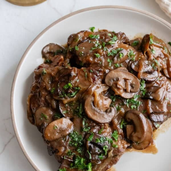 round steak topped with mushrooms on a plate.