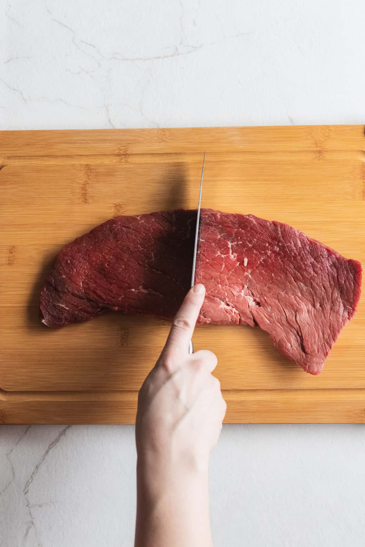 cutting round steak into two pieces on a cutting board.