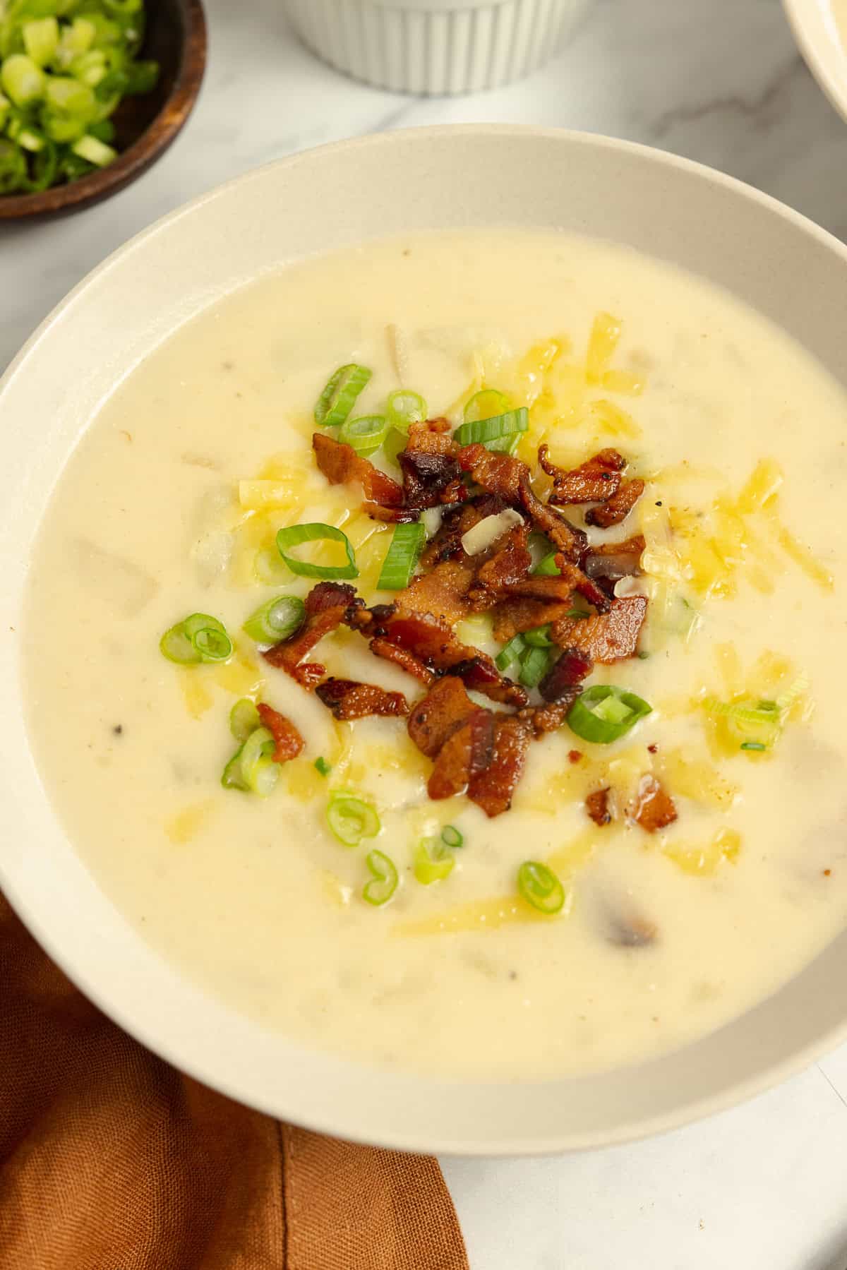 Close up of a bowl of loaded potato soup topped with cheese, green onion, and chopped bacon.