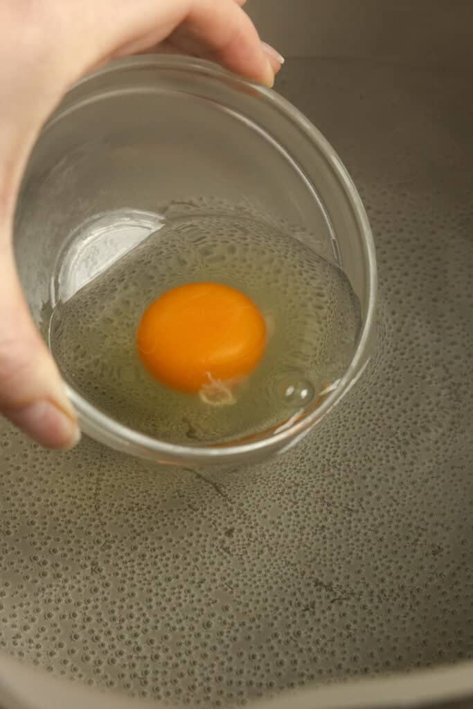 Egg in a bowl being poured into a pot of water.