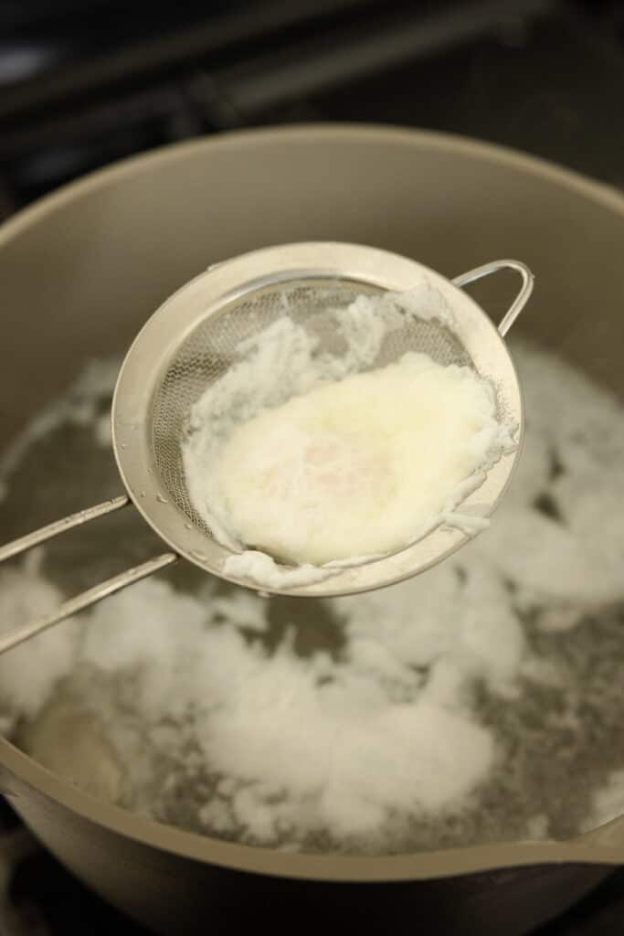 Using a fine mesh strainer to remove a poached egg.