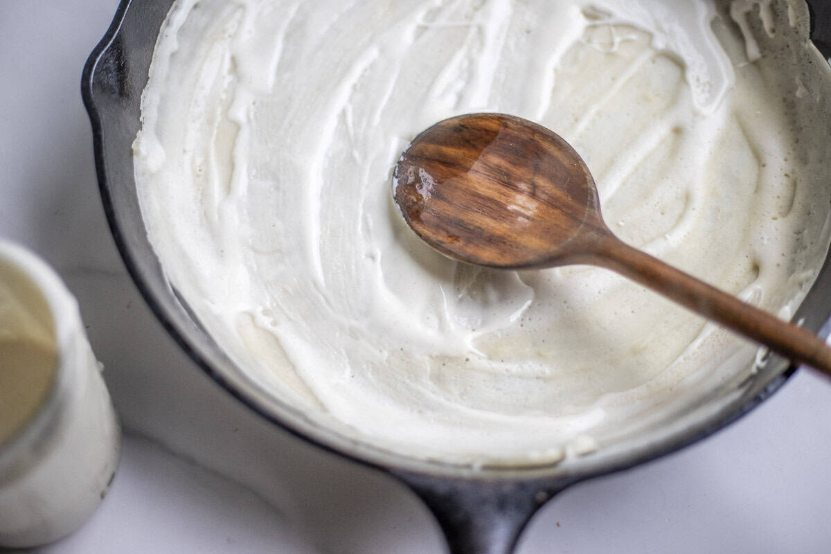 Sourdough discard spread out on a cast iron skillet with a wooden spoon.