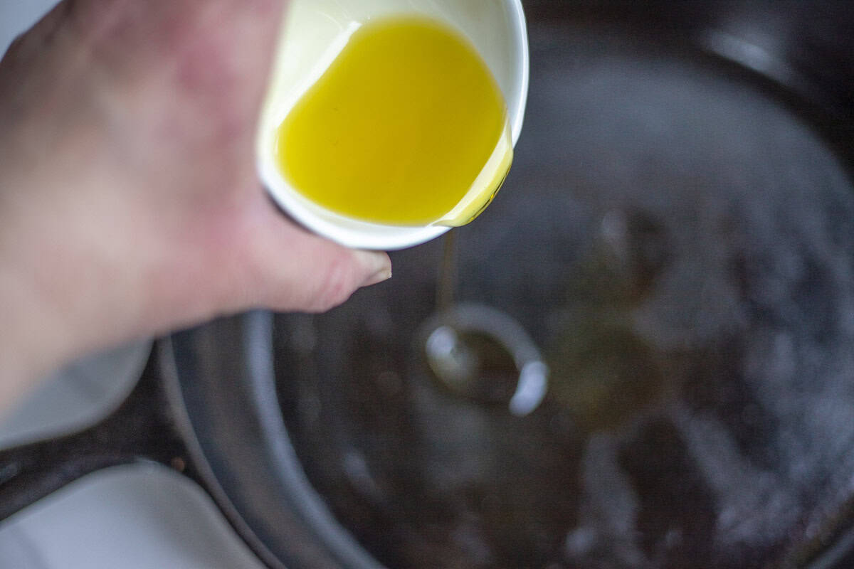 Olive oil added to a hot cast iron skillet.