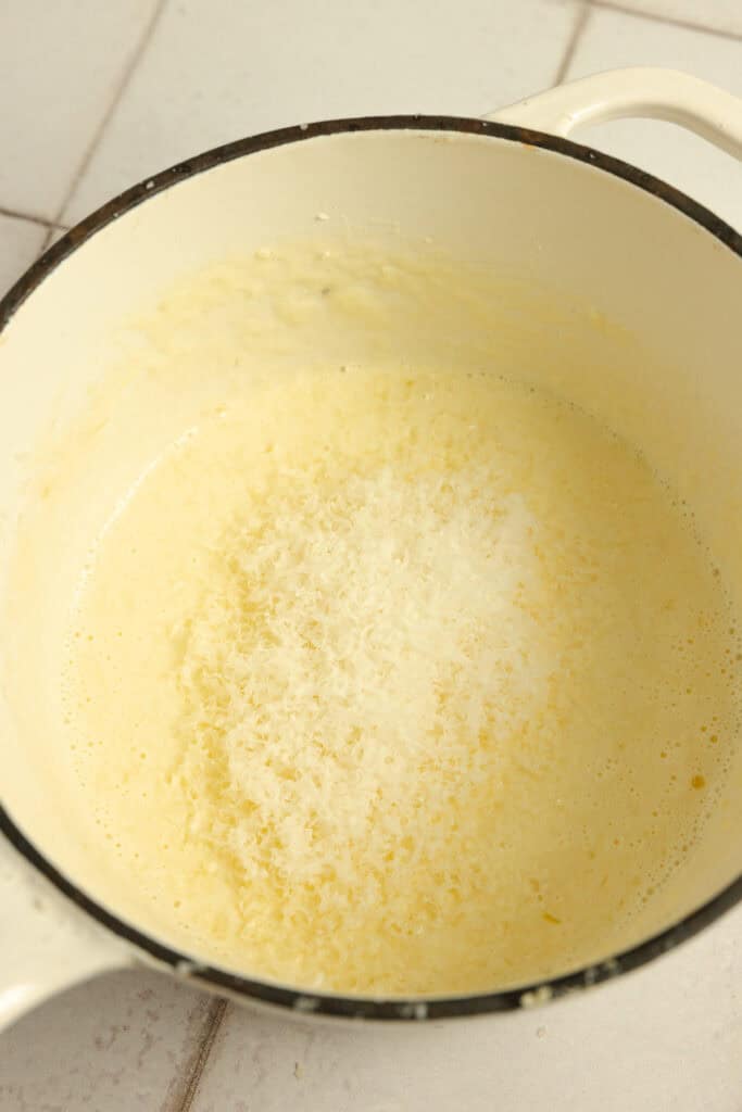 Grated parmesan added to a sauce pot of butter and cream.
