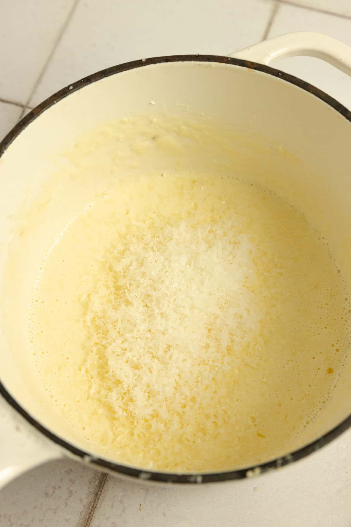 Grated parmesan added to a sauce pot of butter and cream.