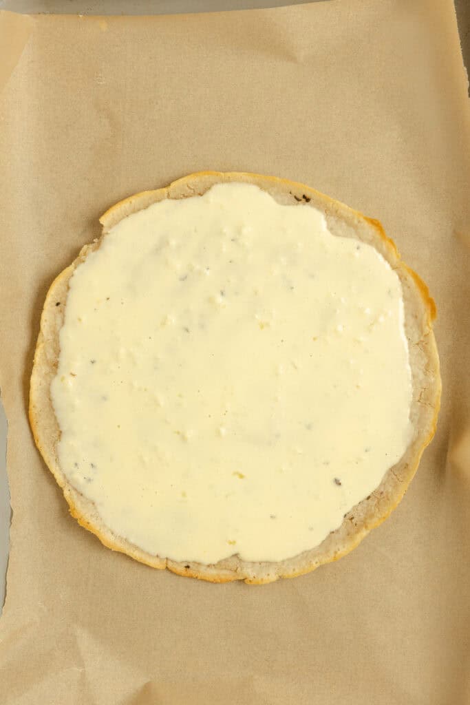 Pizza crust on parchment paper with sauce.