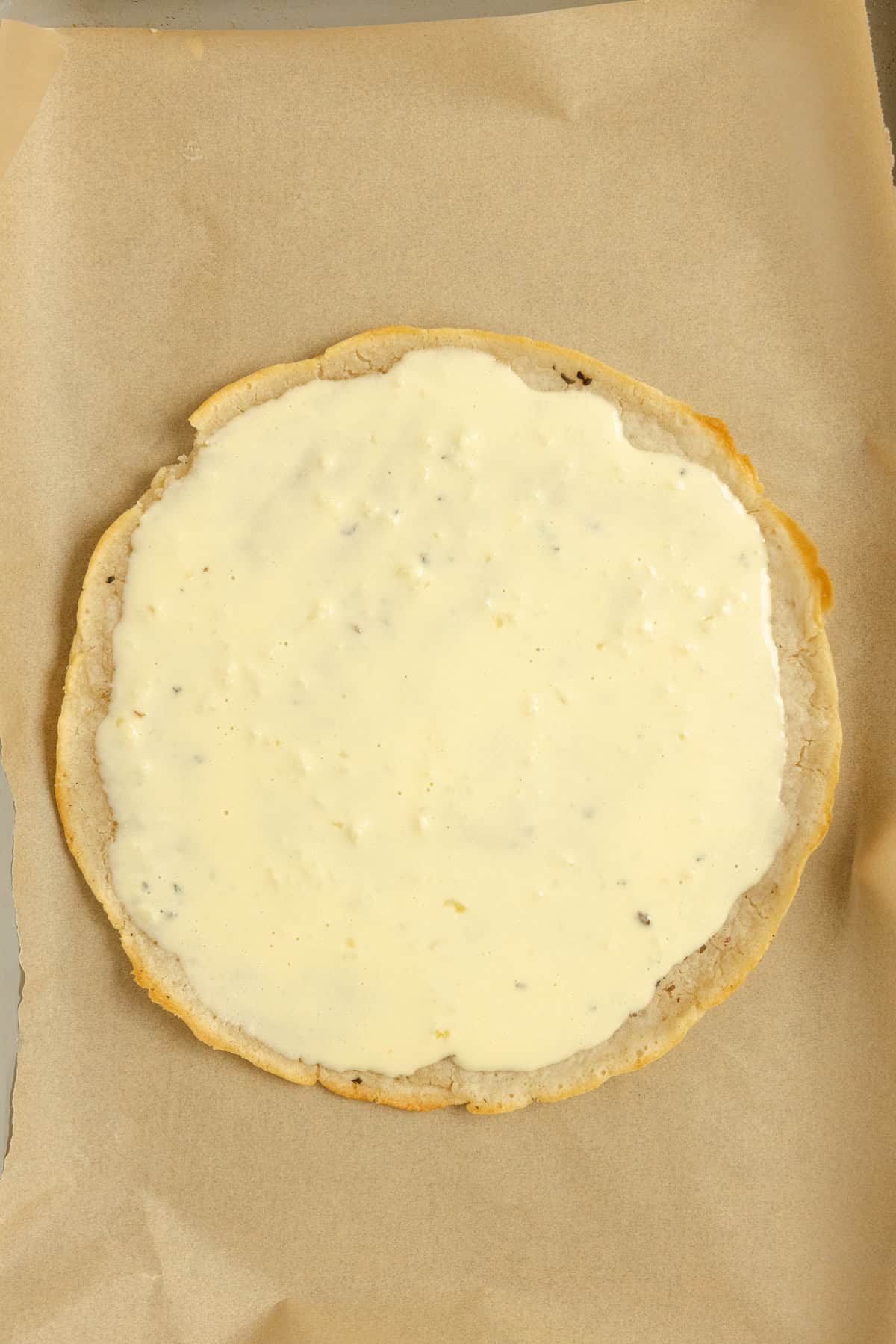 Pizza crust on parchment paper with sauce.