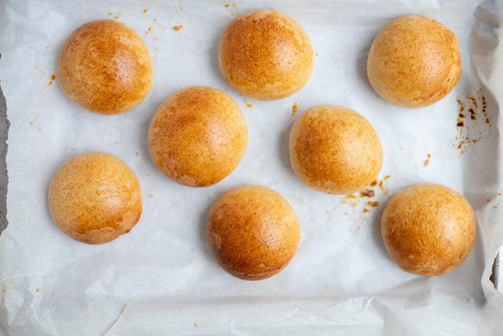 Freshly baked whole wheat sourdough dinner rolls on a parchment lined baking sheet.