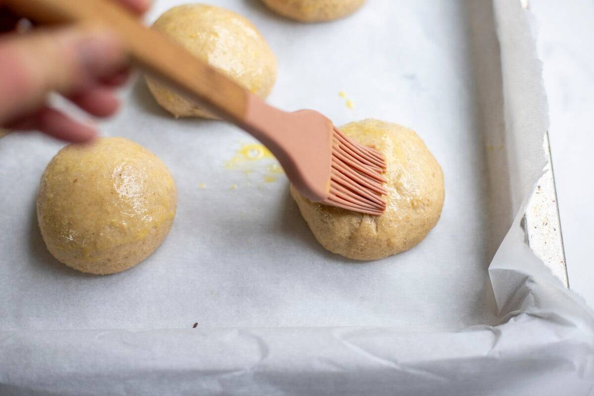 Adding egg wash to the tops of rolls.