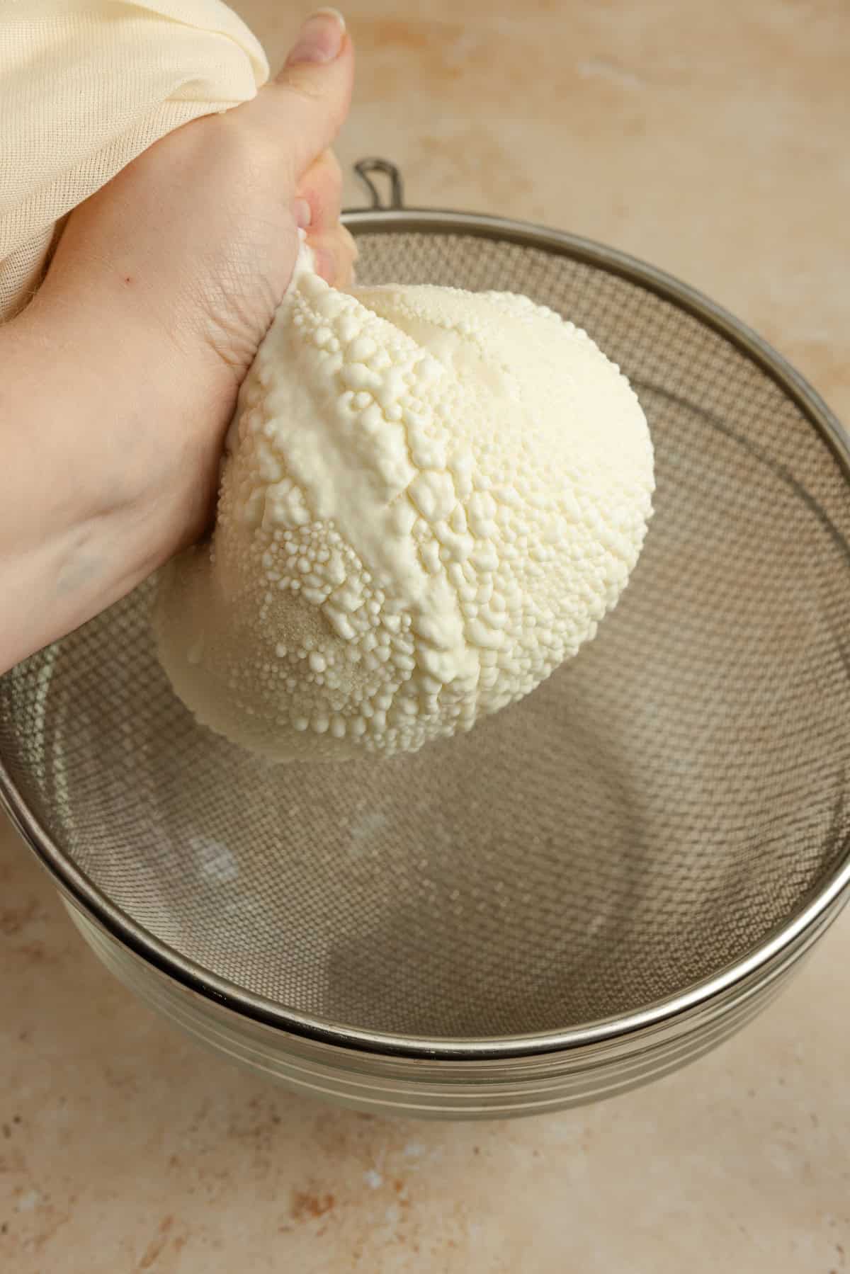 A hand squeezing a cheese cloth full of yogurt.