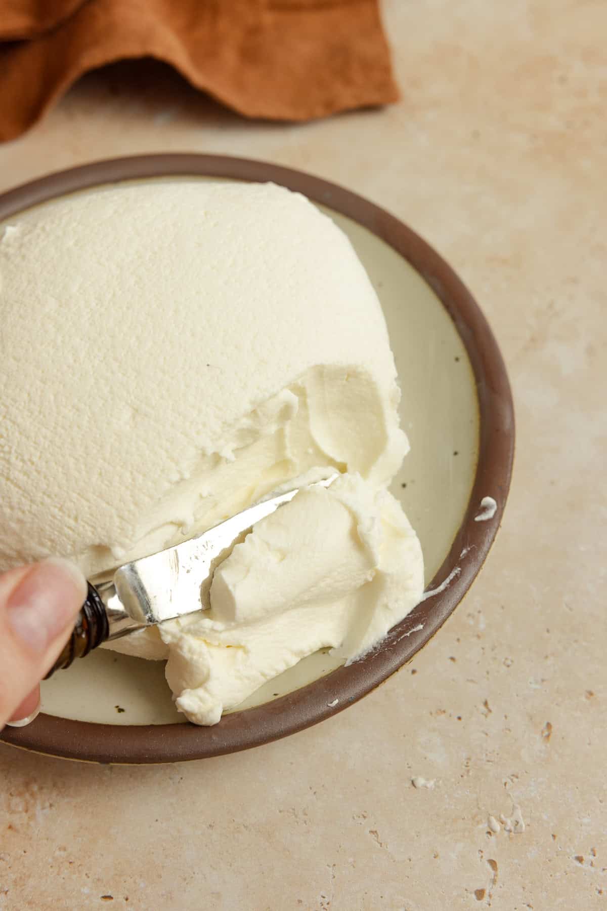 A plate of yogurt cheese with a knife cutting into it.
