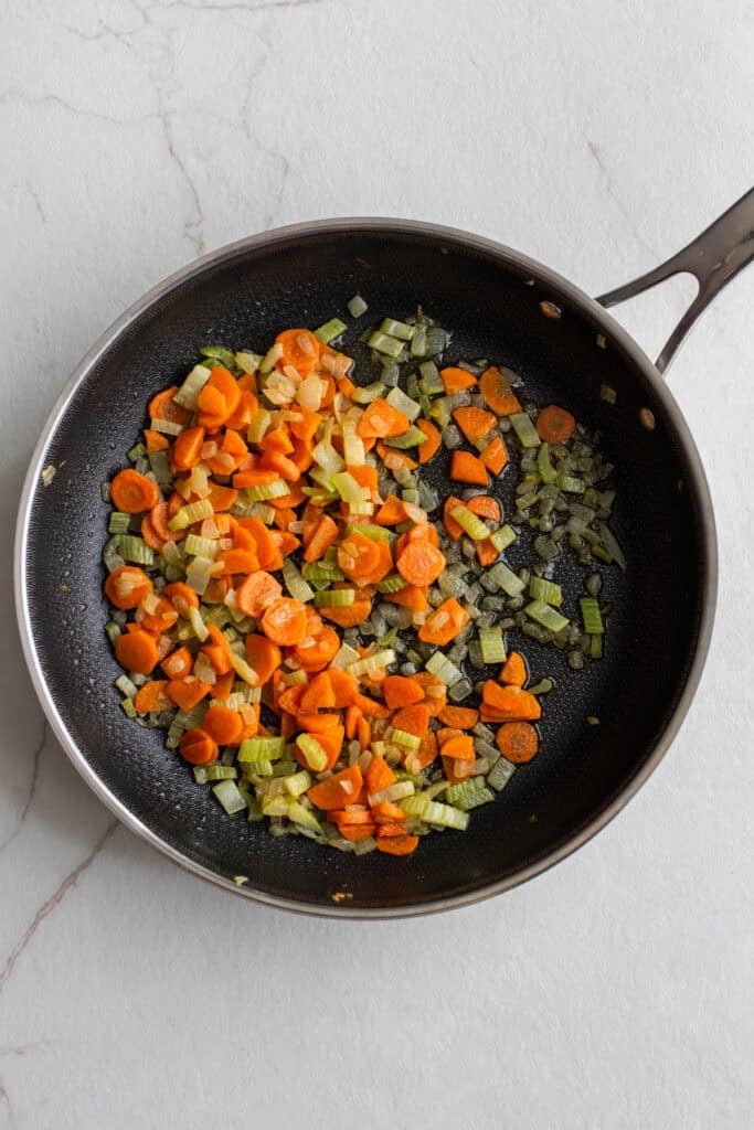 Celery, carrots, and onions being sautéed with butter in a skillet.