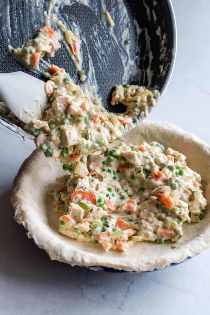 Chicken pot pie filling pouring into an unbaked pie crust.