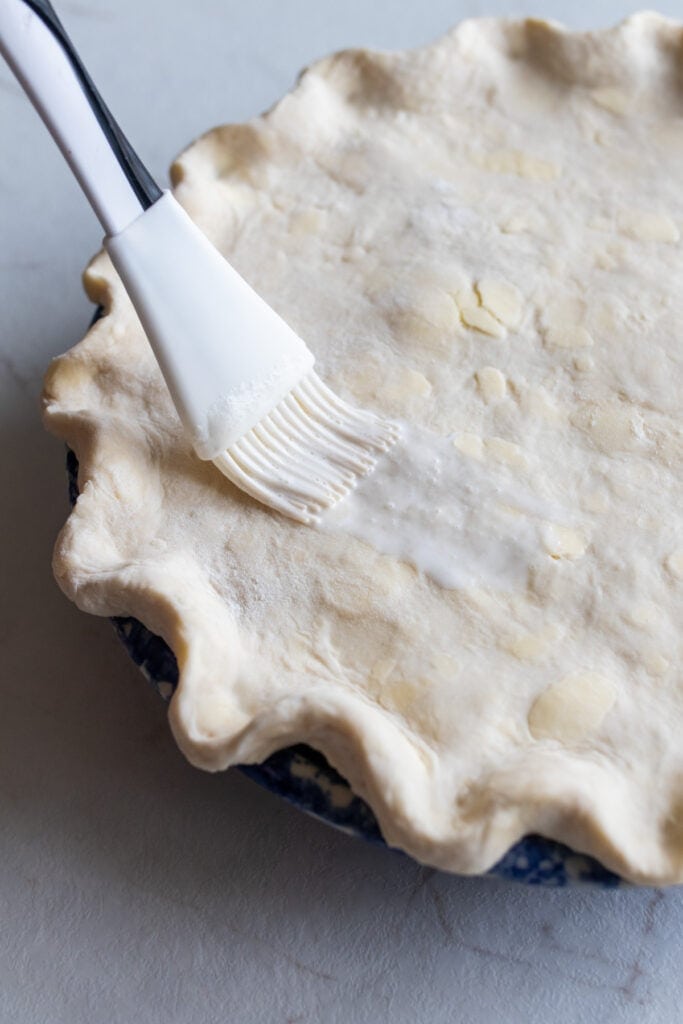 A pastry brush covering a pie crust in an egg wash.
