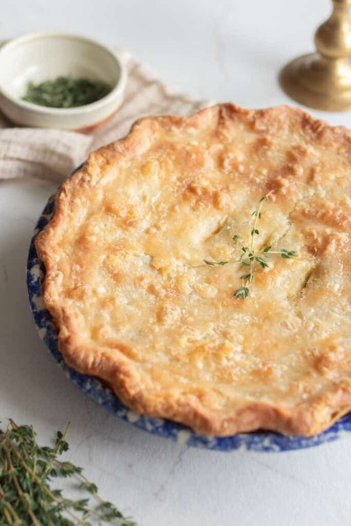 A freshly baked chicken pot pie sitting on the counter top by garnishes in a bowl.