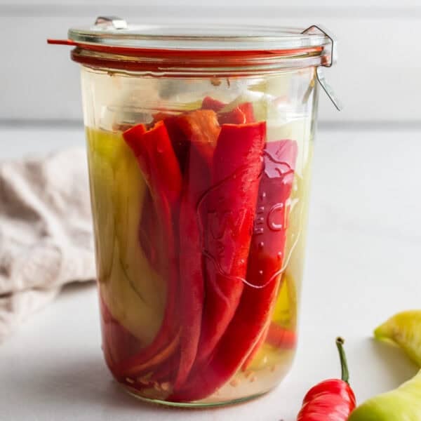 Fermented peppers in a jar with fresh peppers in front of the jar.