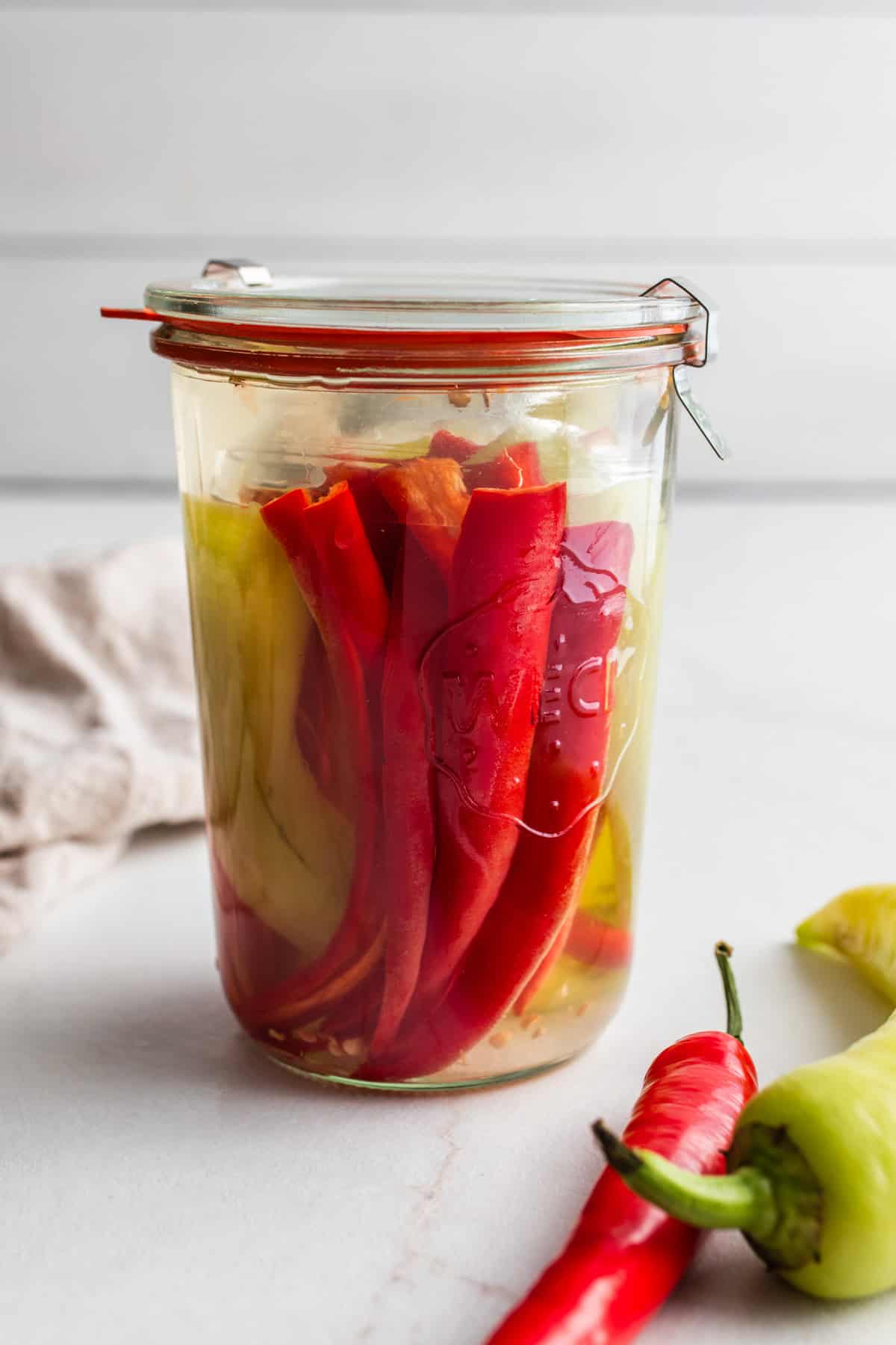 Fermented peppers in a jar with fresh peppers in front of the jar.