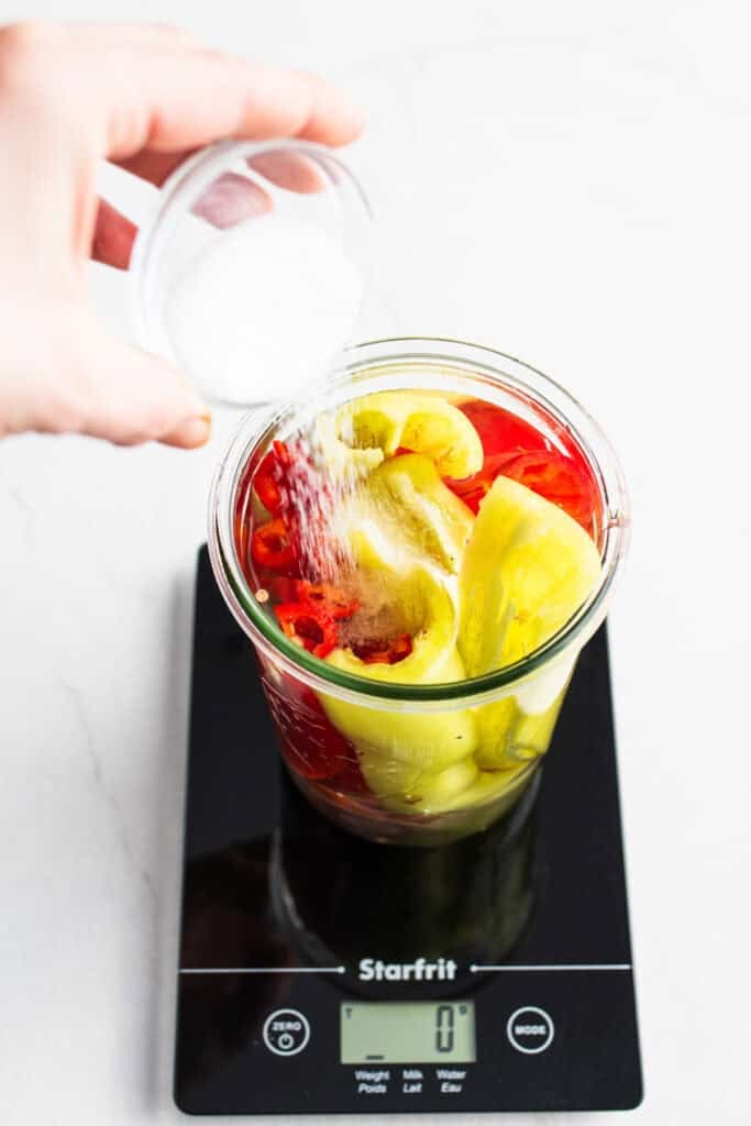 Salt being added to water and sliced peppers in a jar.