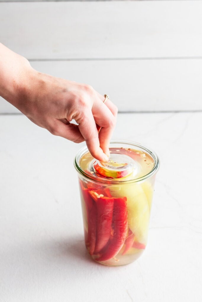 Adding fermentation weight peppers in a brine solution in a glass jar.