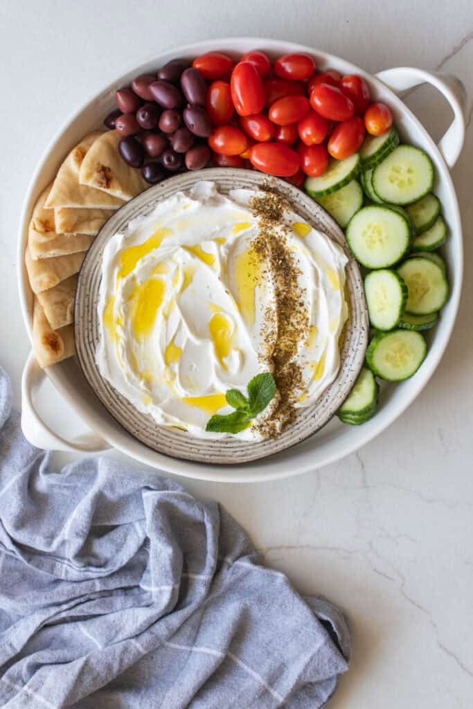 Labneh on a plate surrounded with vegetables and pita chips.