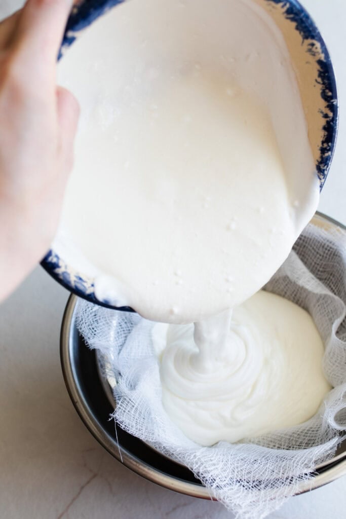 Yogurt being poured over a strainer and cheesecloth.