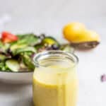 Lemon dressing in a glass jar with a salad and two lemons in the background.
