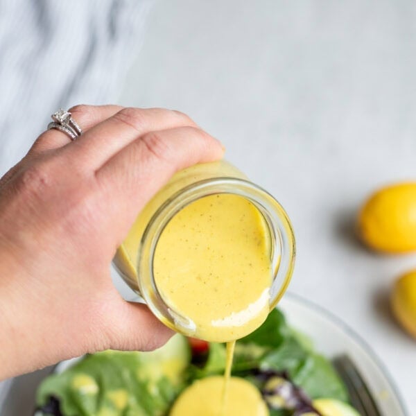 Pouring lemon Vinaigrette dressing over a salad with cucumber slices.