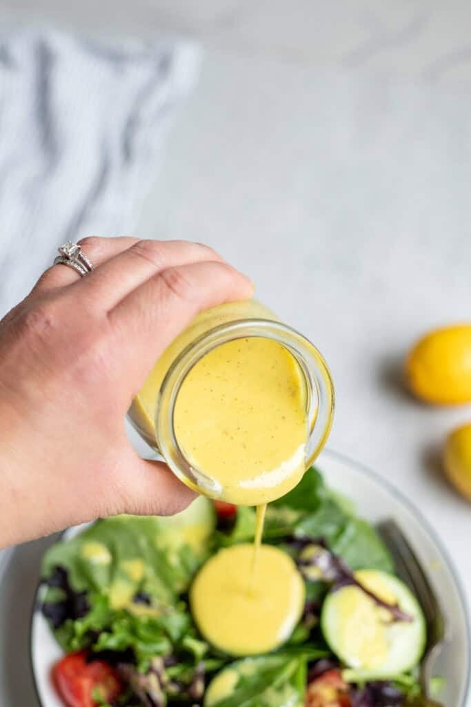 Pouring lemon Vinaigrette dressing over a salad with cucumber slices.