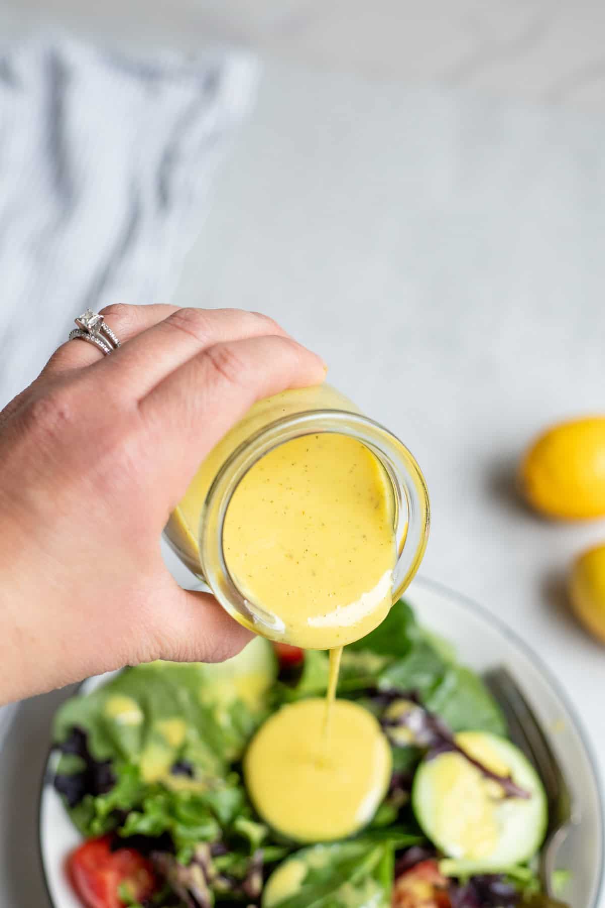 Pouring lemon vinaigrette dressing over a salad with cucumber slices.