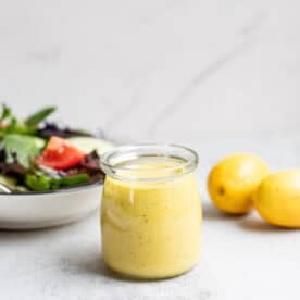 Lemon vinaigrette dressing in a glass jar with a salad and lemons in the background.