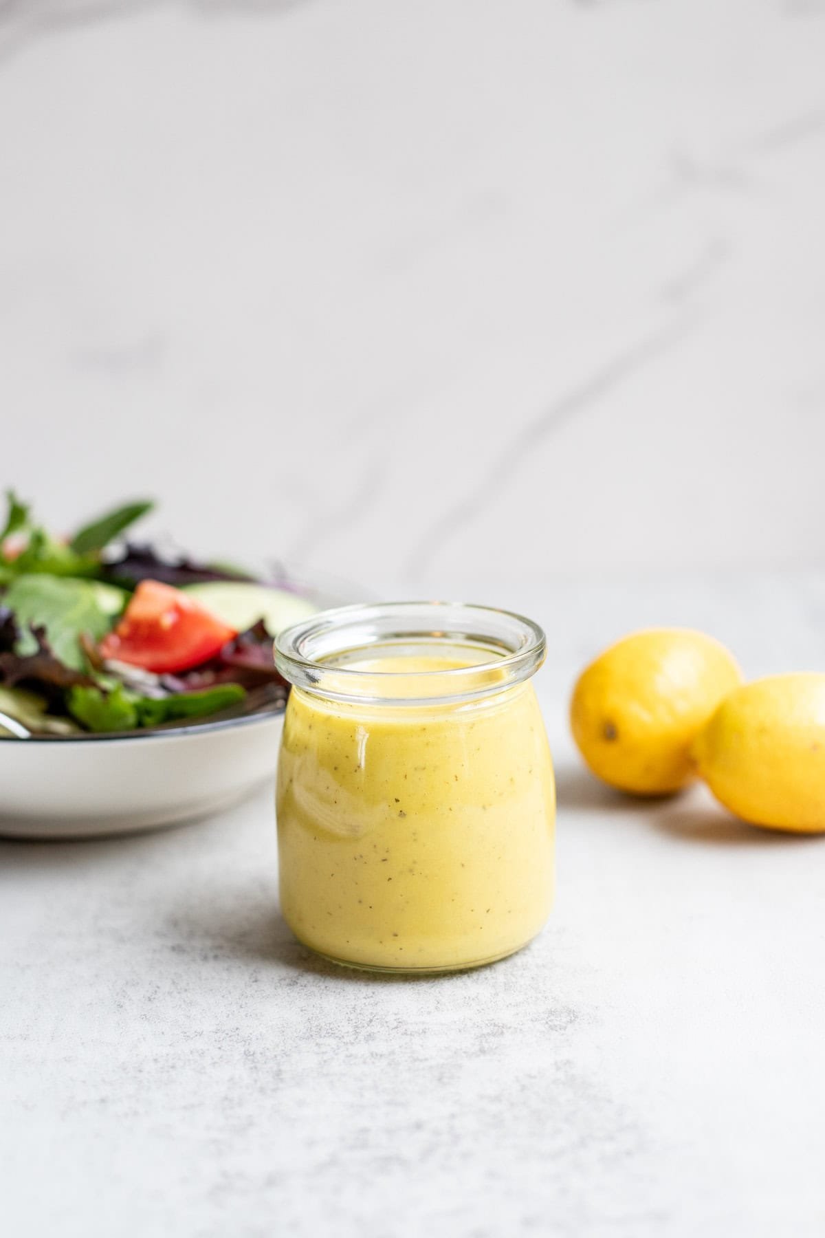 Lemon vinaigrette dressing in a glass jar with a salad and lemons in the background.