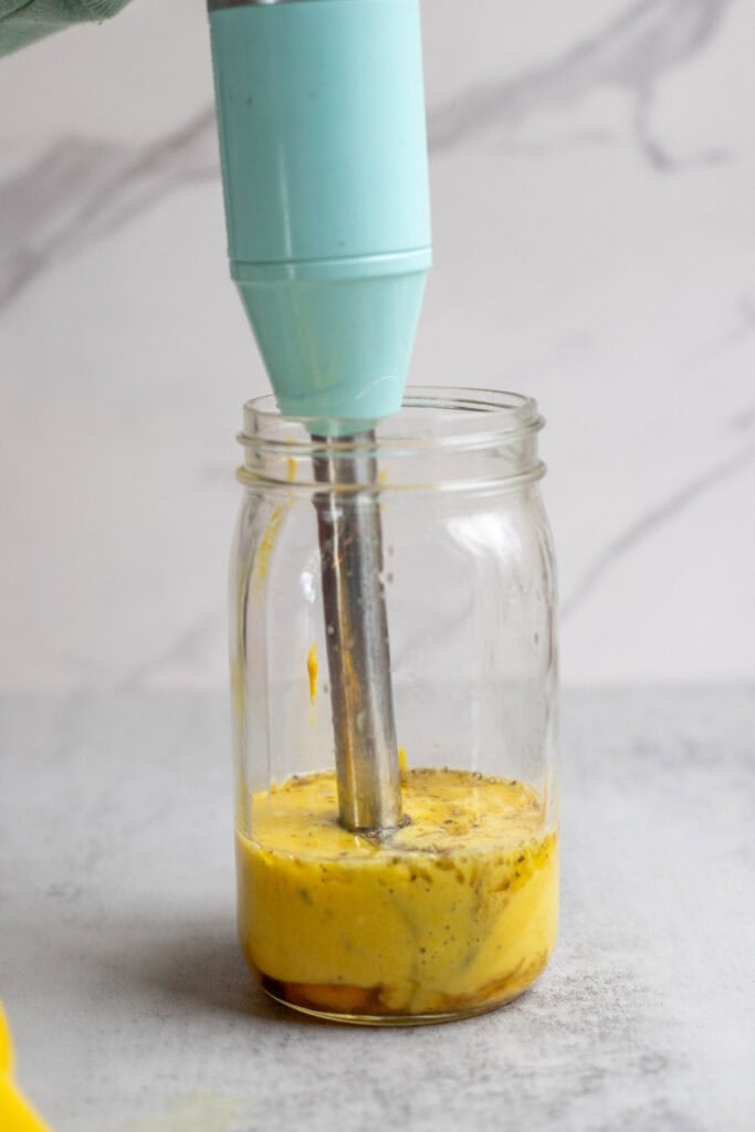 Blending lemon dressing in a mason jar with an immersion blender.