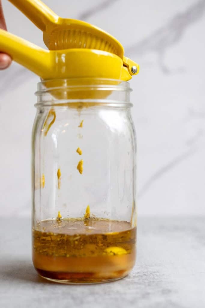 Squeezing lemon juice into a jar of mustard, oil, and apple cider vinegar.