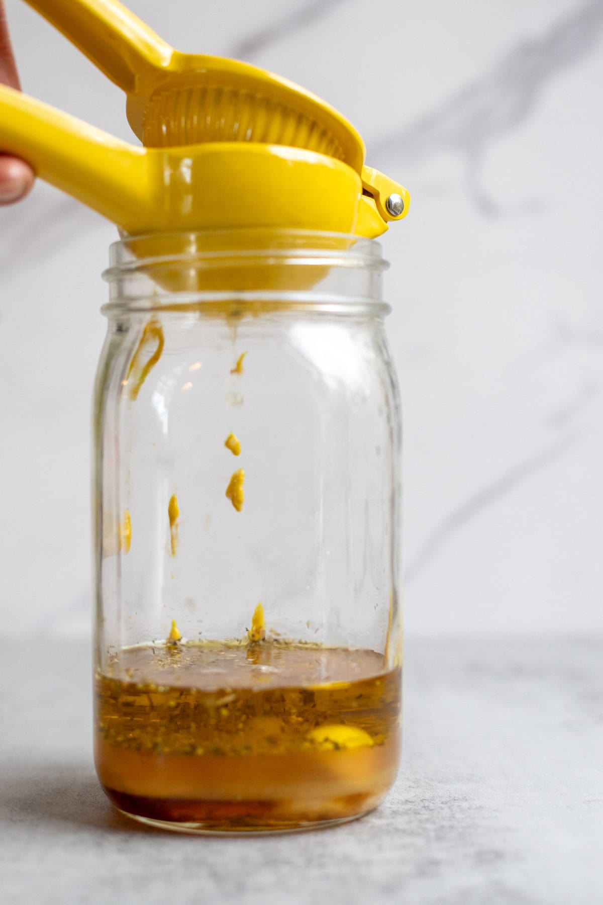 Squeezing lemon juice into a jar of mustard, oil, and apple cider vinegar.