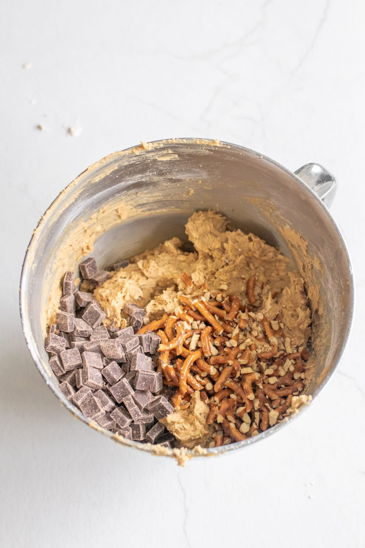 Folding pretzels and chocolate chips into cookie dough in a bowl.