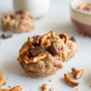 lactation cookies made with oats, pretzels and chocolate chips on a white countertop with a glass of milk in the background.