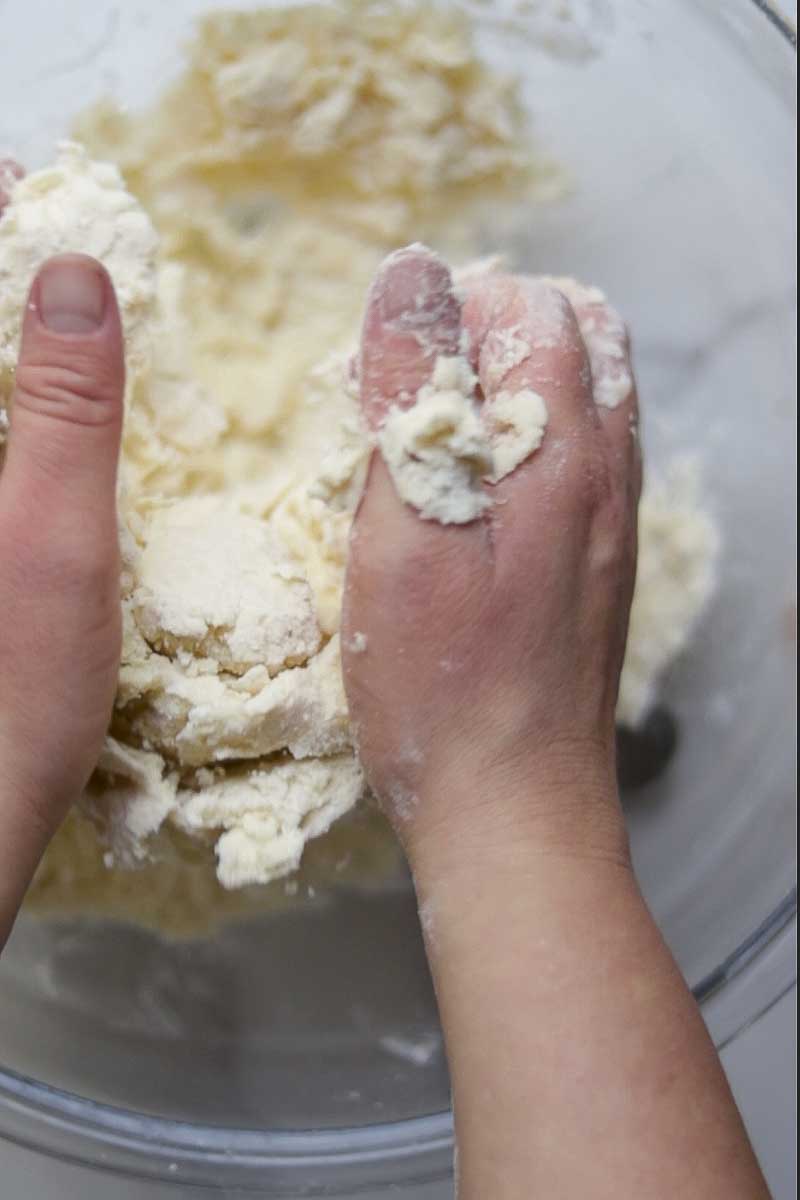 Hands kneading together a butter and flour to make a pie crust.