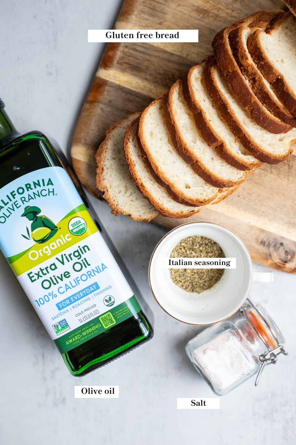 Sliced gluten free bread on a cutting board, a jar of salt, small bowl of seasonings and jar of olive oil on a countertop.
