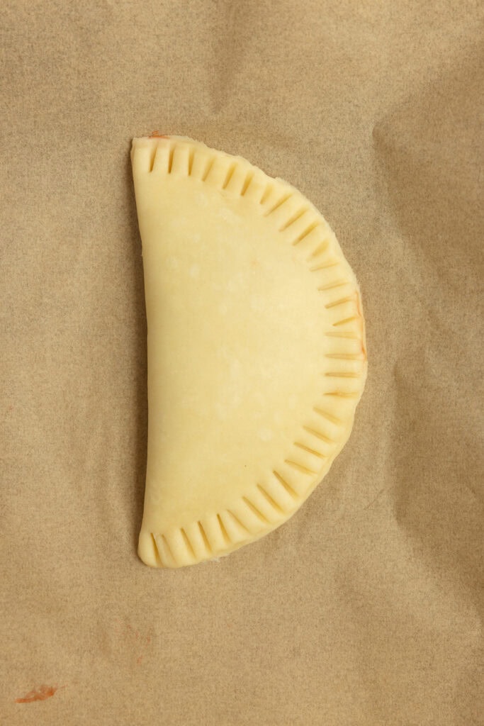 Hand pie with the edges crimped on parchment paper.