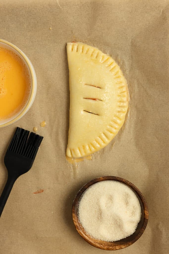 Raw hand pie with an egg wash sprinkled with sugar.