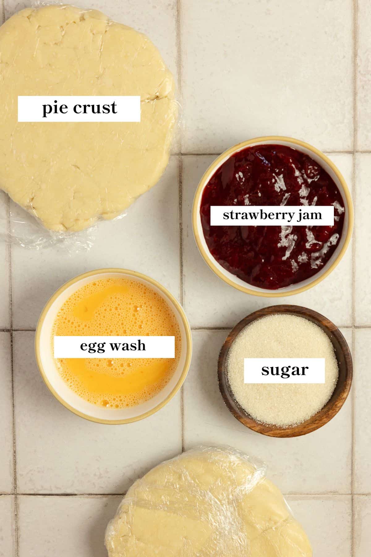 Pie dough, strawberry jam, sugar, and an egg wash on a countertop.