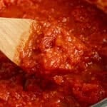 pasta sauce being spooned out of a pot with a wooden spoon.