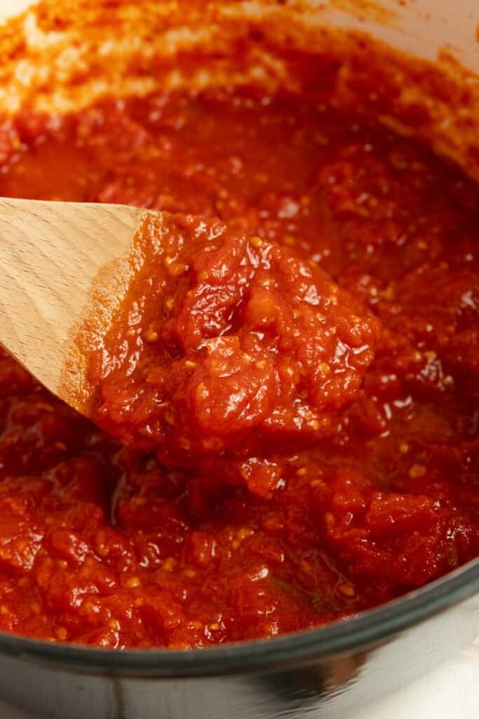Pasta sauce being spooned out of a pot with a wooden spoon.