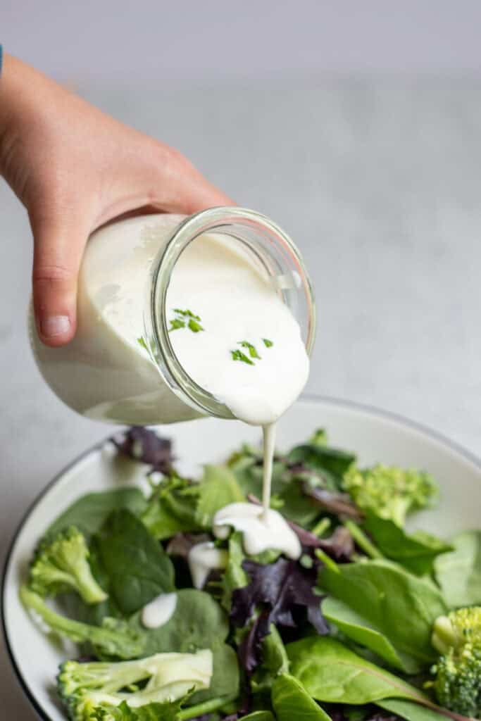 Pouring ranch dressing over a salad.
