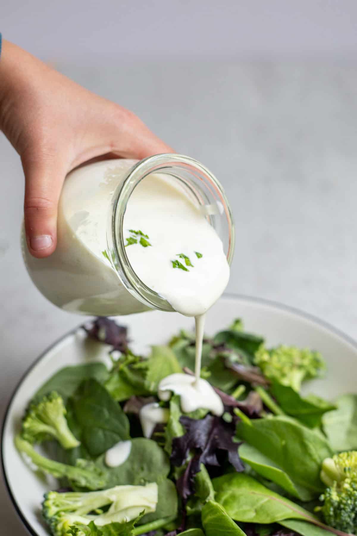 Pouring ranch dressing over a salad.